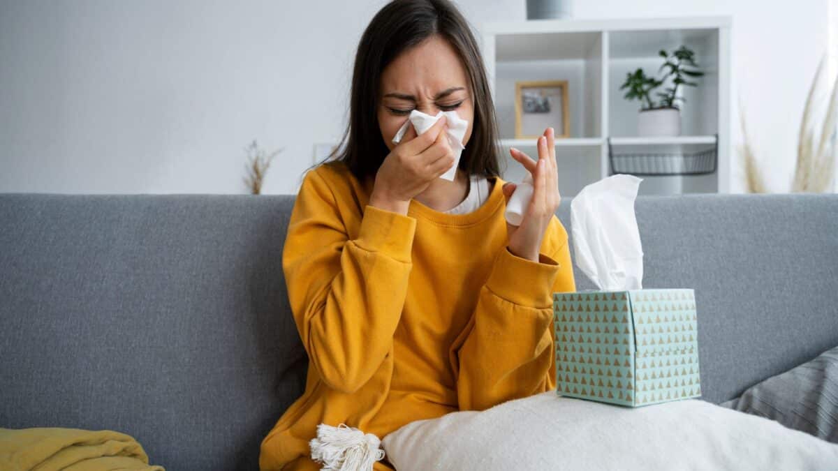 Struggling with fluctuating hormones and allergies, a woman sneezes and wipes her nose.