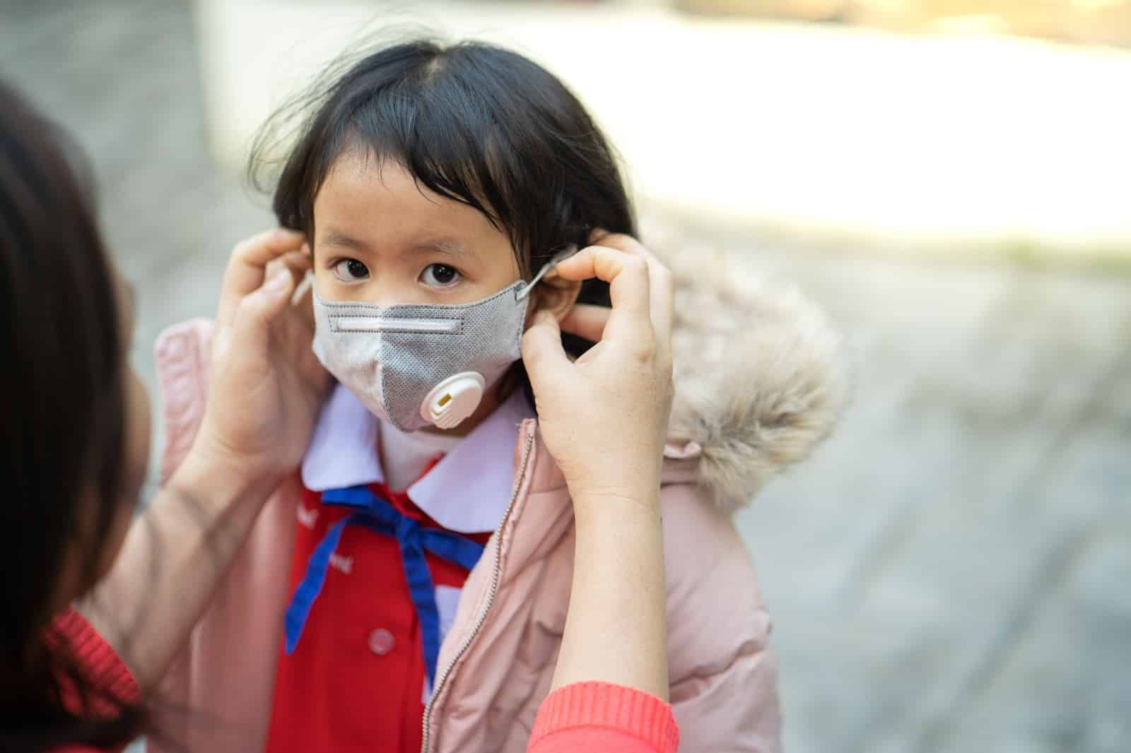 A woman puts an N95 mask on her toddler to manage summer allergies.