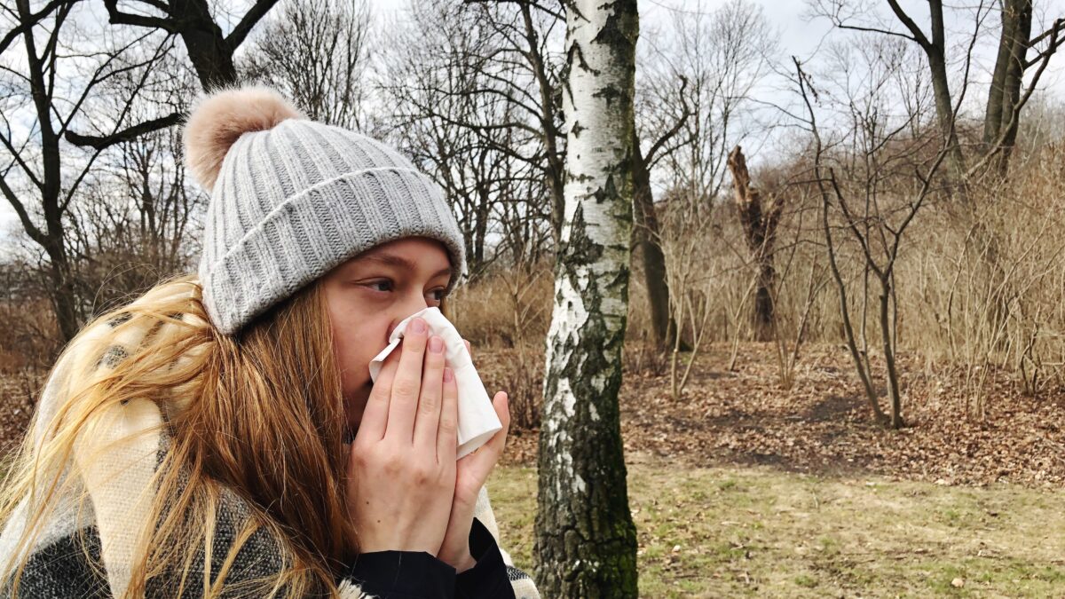 A woman wipes her nose as she suffers from fall cold season allergies.
