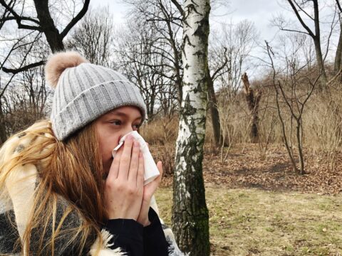 A woman wipes her nose as she suffers from fall cold season allergies.