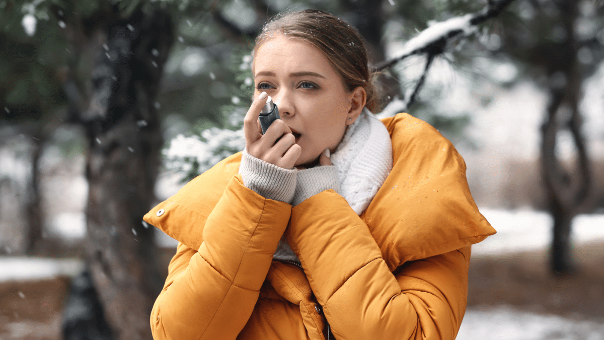 While taking a walk in the snow, a woman uses her inhaler as she experiences asthma flare-ups in winter.
