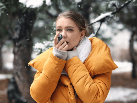 While taking a walk in the snow, a woman uses her inhaler as she experiences asthma flare-ups in winter.